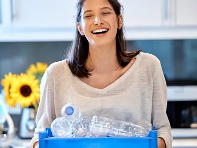 A person holds a blue box full of recycling.